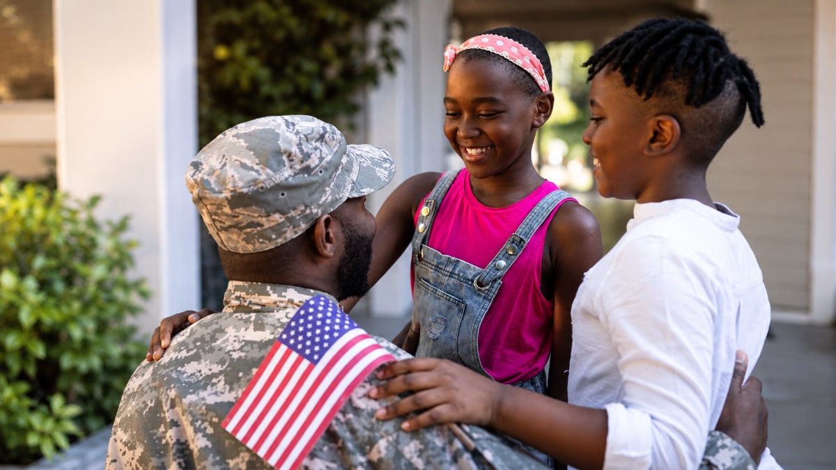 A soldier in uniform embracing his two smiling children